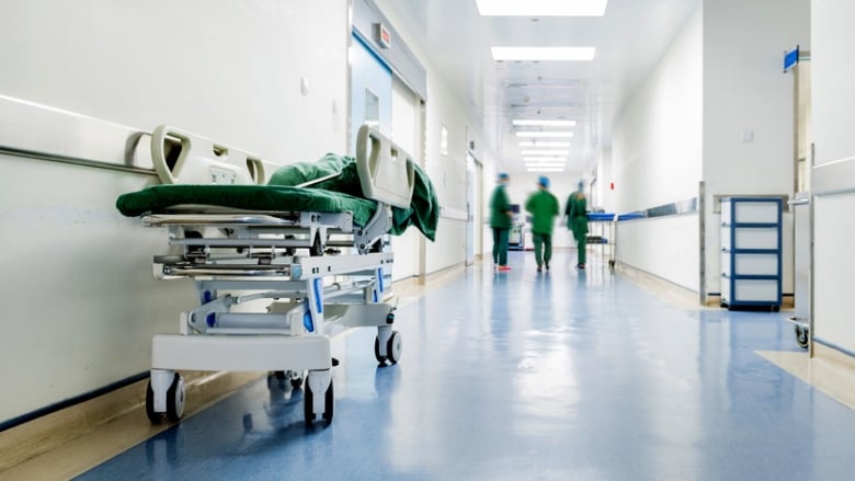 A bed stretcher in a hall. People in scrubs can be seen walking down the hall.