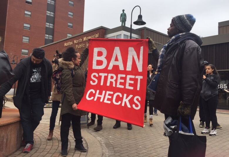 A group of people stand in front a library holding a sign that says 