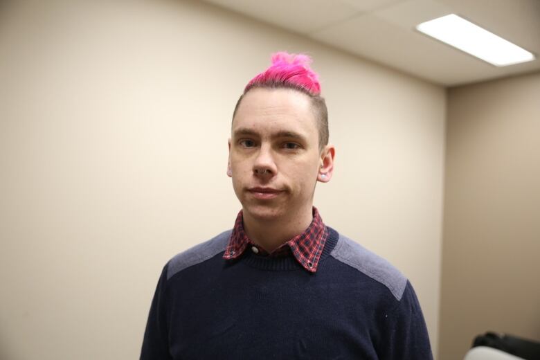 A person wearing a sweater stands in front of a beige wall.