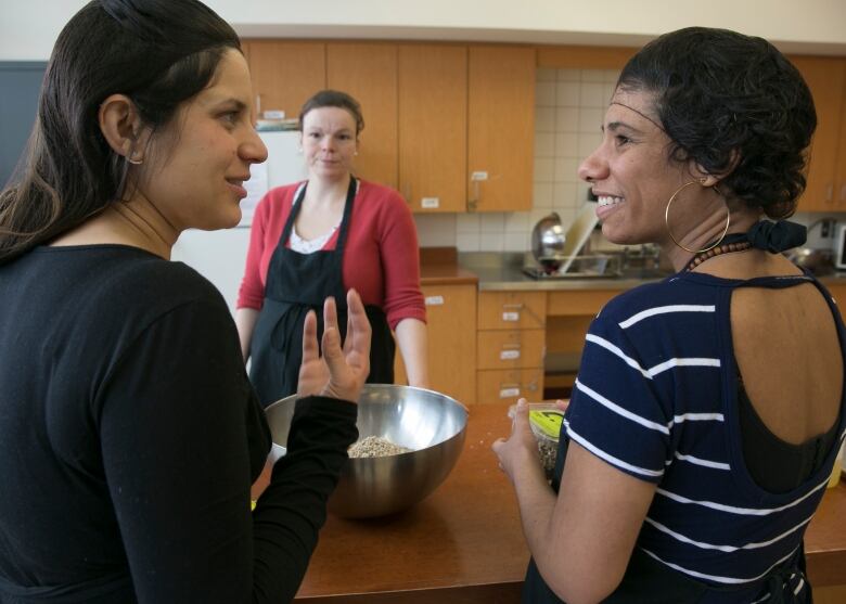 Three women talk while cooking.