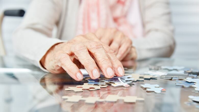 Close up on hands of older woman working on a jigsaw puzzle.