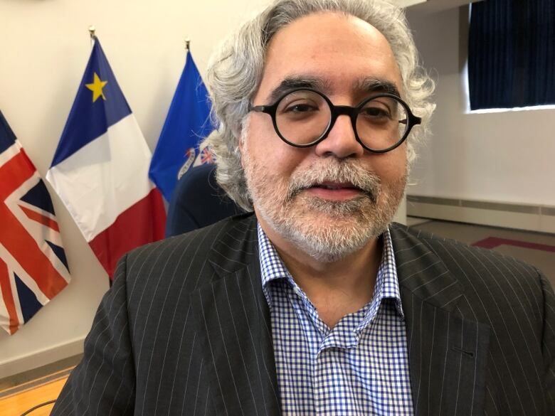 A man wearing glasses with flags in the background.