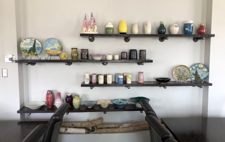 Four staggered, floating shelves are lined with colourful pottery of various shapes and styles, from vases to mugs to plates to bowls.