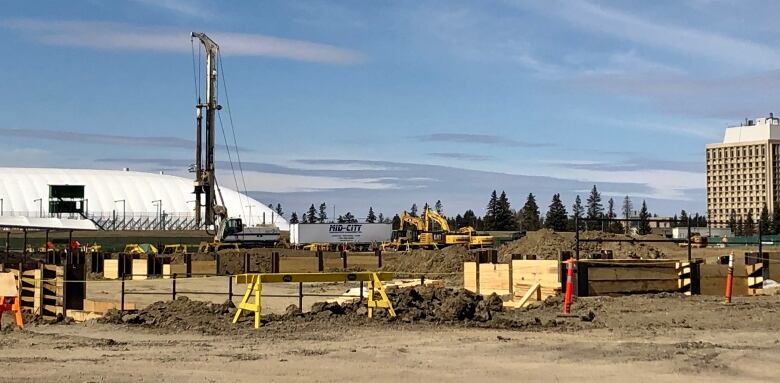 A crane towers over an halted construction site showing piles of dirt and machinery. There are no workers.