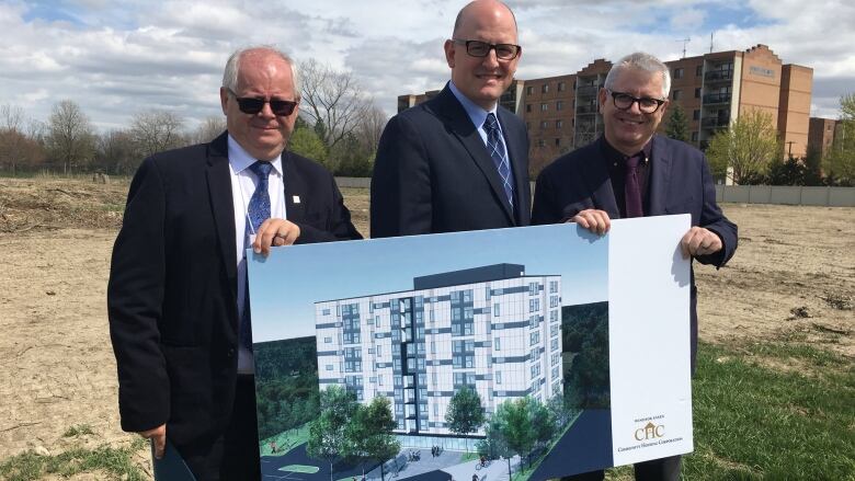 Three men in suits with a photo of an apartment building. 