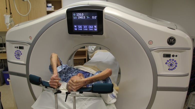 A person lying on a bed is seen waiting in a CT scan.