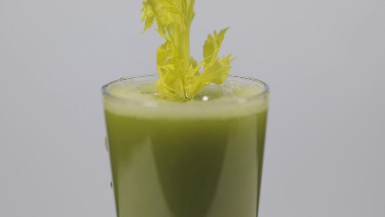 Celery leaves stick out from the top of a glass filled with green juice.