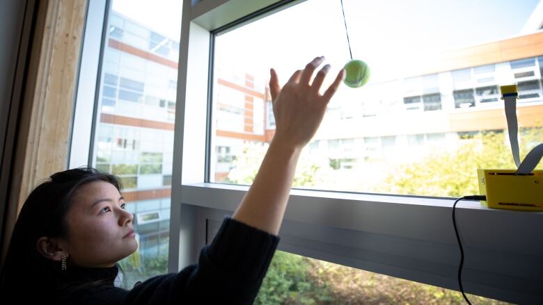 A woman points up to a tennis ball hung on a glass window.