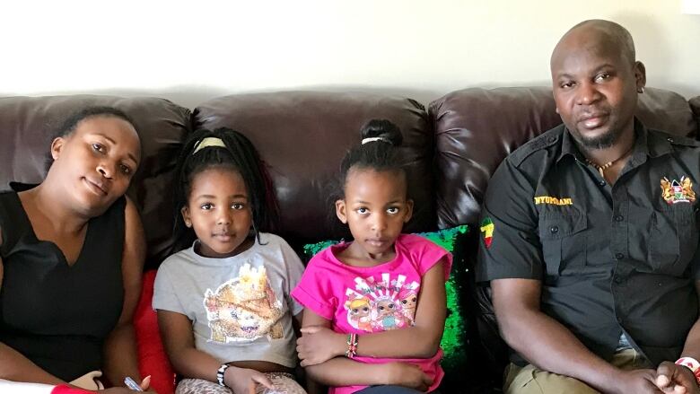 A family of four sits on a couch with the two children sitting between the adults.