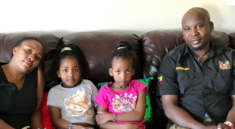 A family of four sits on a couch with the two children sitting between the adults.