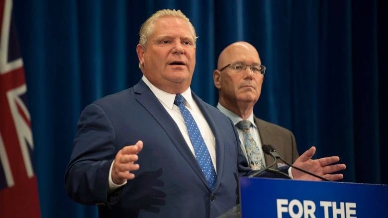 Two men speak at a press conference behind a podium sign that reads 