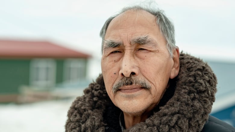 A man wearing a parka is seen in a close up looking at the camera. 