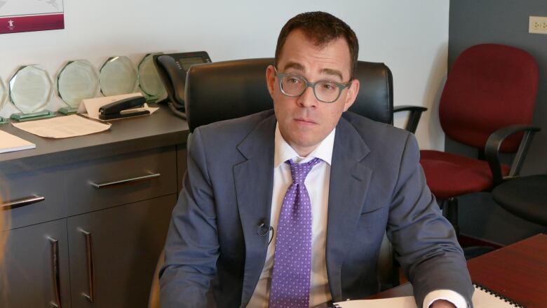 A man sitting at a desk in a suit with glasses.