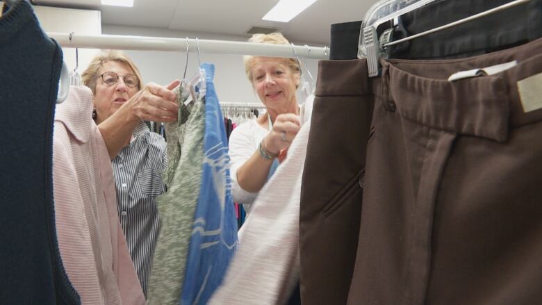 Two women hanging piles of used clothes. 