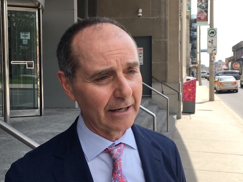 A man in a suit speaks on a city street.