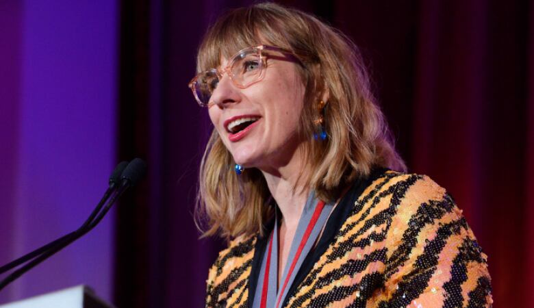 A woman wearing a patterned, sequined top speaks at a podium.