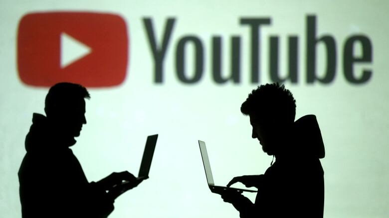 Silhouettes of two people holding laptops in front of the YouTube logo