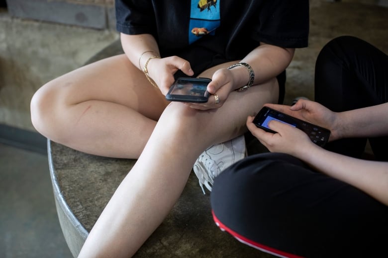 High school students, their faces unseen, sit cross-legged on concrete steps while scrolling on cellphones