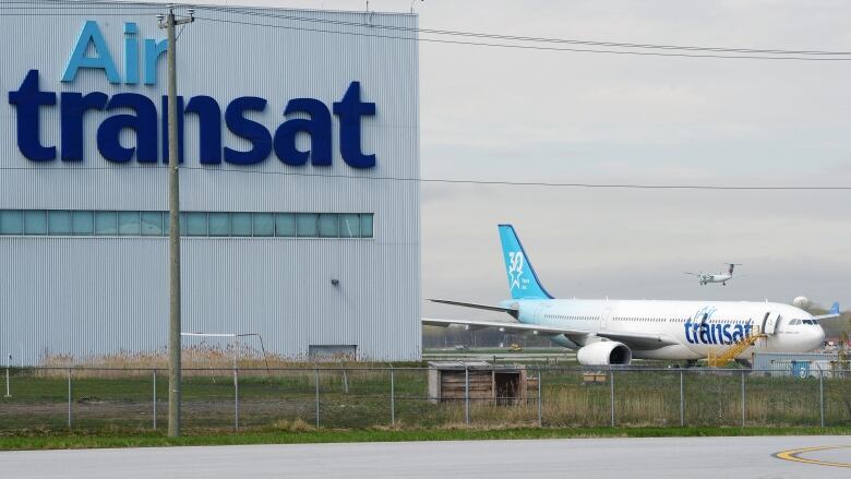 A passenger plane is parked next to a hanger. Both are protected by a tall fence with barbed wire on top.