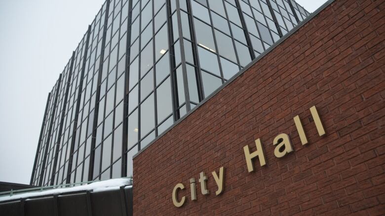 A tall glass building stands over a shorter brick building that has a sign reading 'city hall'