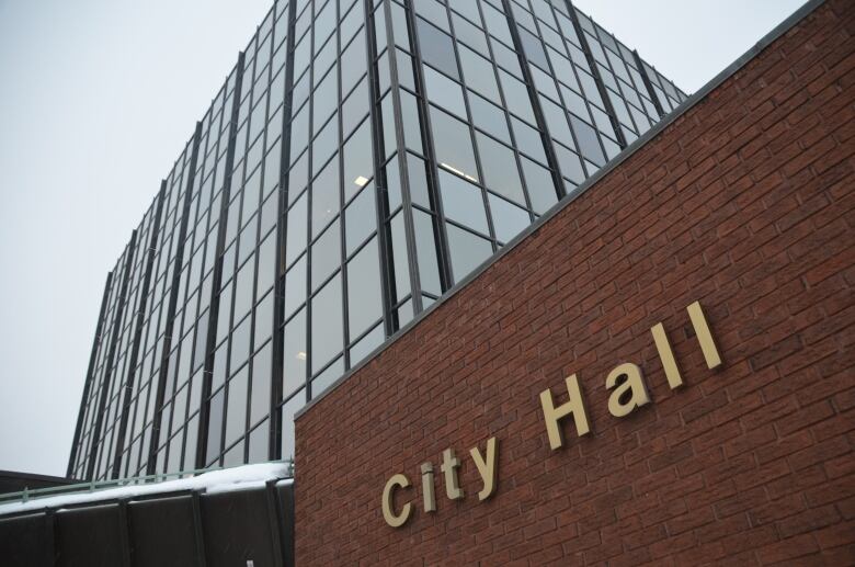 A tall glass building stands over a shorter brick building that has a sign reading 'city hall'