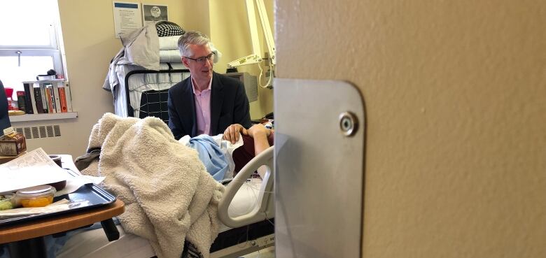 A man is shown sitting next to a hospital bed.