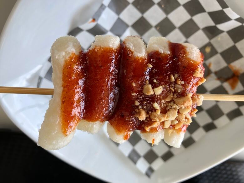 Small white cylinders skewered on a stick and coated in a bright reddish orange sauce.