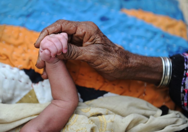 A grandmother holds the hand of their three-day-old grandchild.