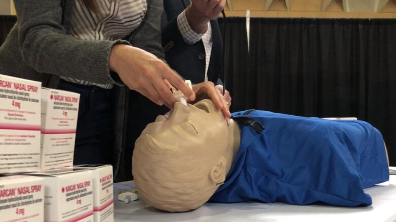 A person is seen administering a nasal spray to a prone mannequin. 