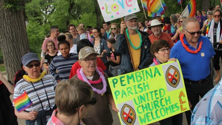 People walk in a Pride parade while carrying signs. 