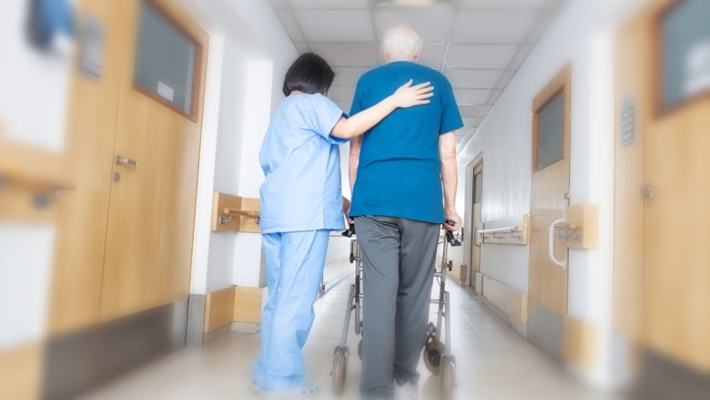 A care worker assists an elderly resident using a walker.