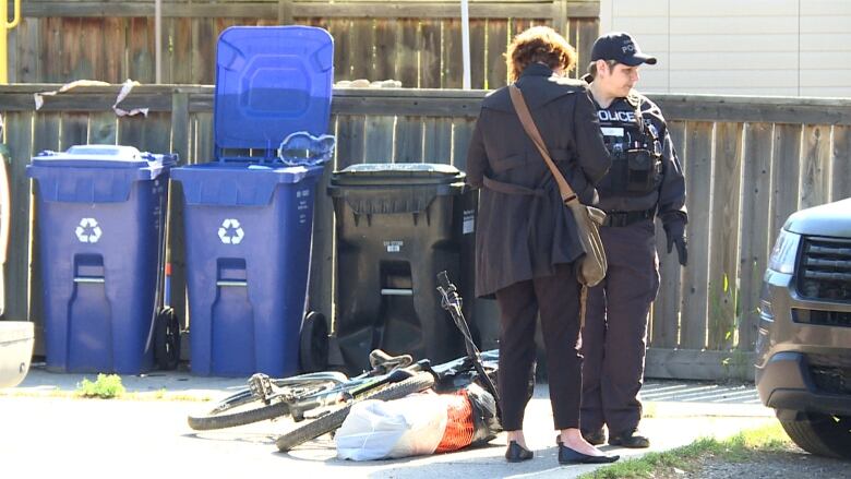 Two people speak in an alley. One is wearing a vest with police written on it.