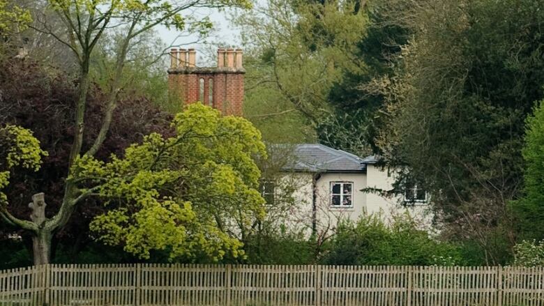 A large house is shown from a distance and behind some trees.