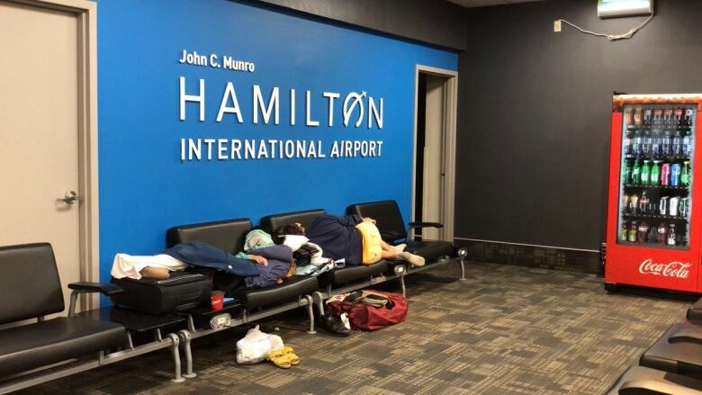 People sleeping on benches in an airport.