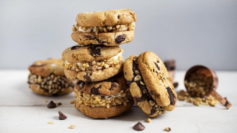 a stack of 3 ice cream sandwiches made with vanilla ice cream and chocolate chip cookies. another sandwich sits beside it and one sits behind it. 