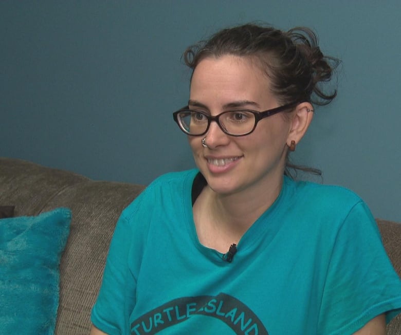 A smiling young woman with her dark hair pulled back, wearing glasses and a T-shirt.