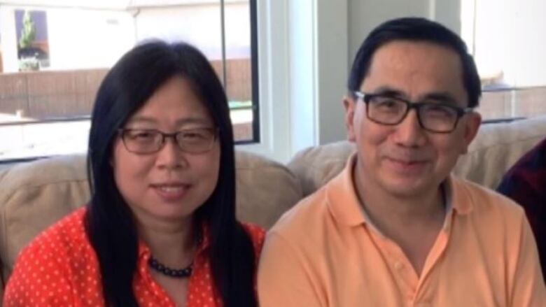 A man and woman sit side by side on a couch, smiling at the camera.