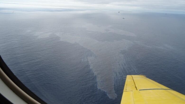 A panoramic photo of the Altantic Ocean through a plane window. A noticeable dark sheen of oil sits on top of the water.