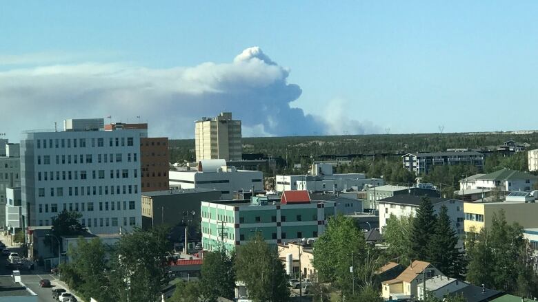 A plum of wildfire smoke is seen in the distance. Yellowknife buildings are visible in the foreground.