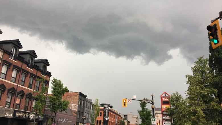 Buildings, cars and part of the road are seen in an intersection as a big, grey cloud covers half of the sky.