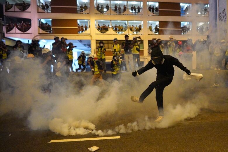 Protester kicks canister with smoke billowing out.