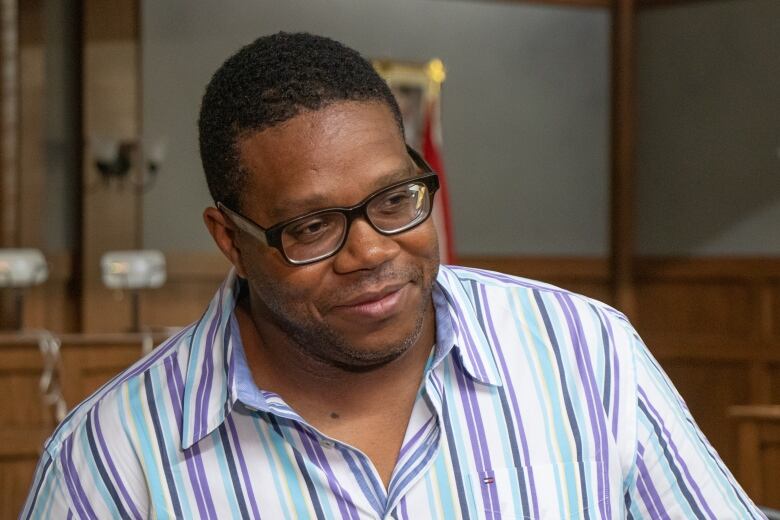 A Black man wearing glasses and a blue and purple stripped shirt