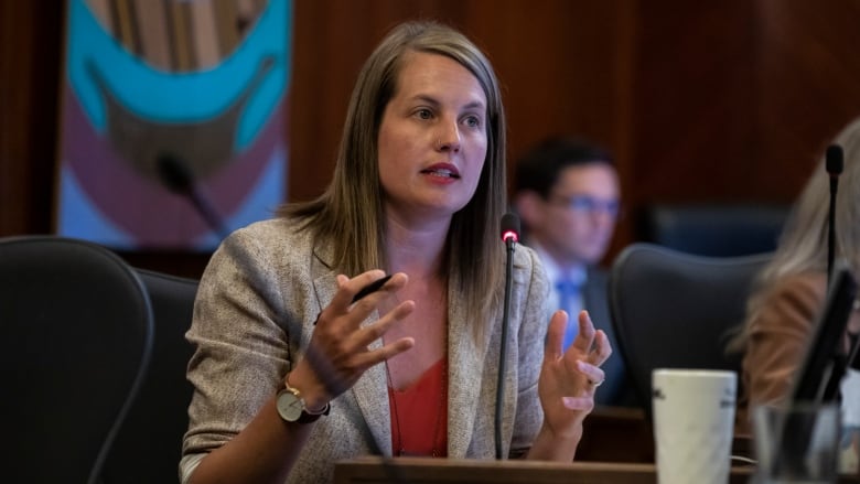 A white woman gestures as she speaks in council.