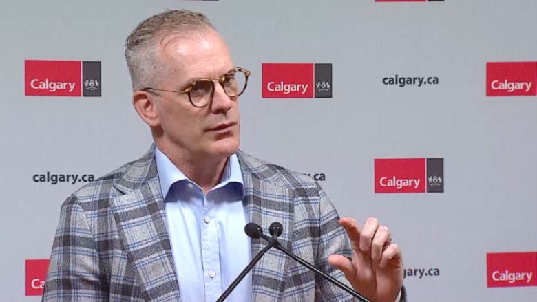 A man speaks in front of a backdrop.