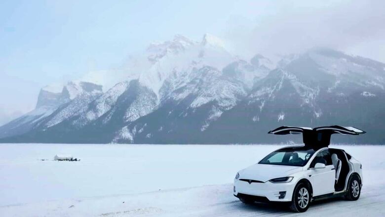 A car is pictured on a snow-covered road with mountain range as its backdrop.