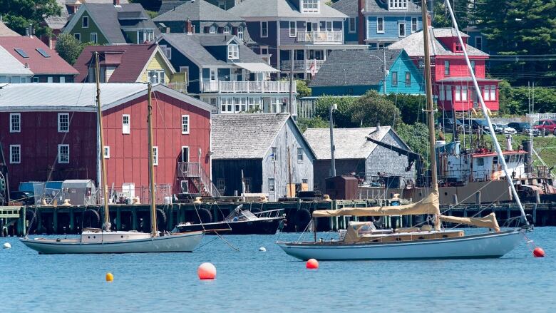 The Lunenburg waterfront is seen with sailboats moored in blue water and wooden buildings on the wharf.