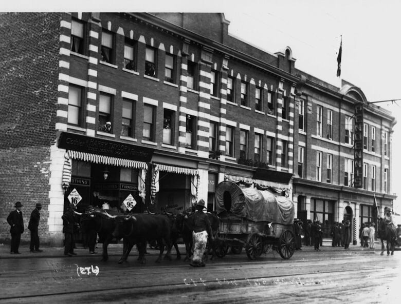 Horses and a buggy are seen outside the brick building in a black and white archival photo.