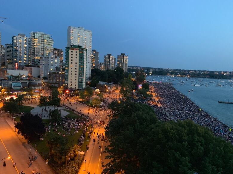 A drone photograph of huge crowds on a beach at twilight in Vancouver.