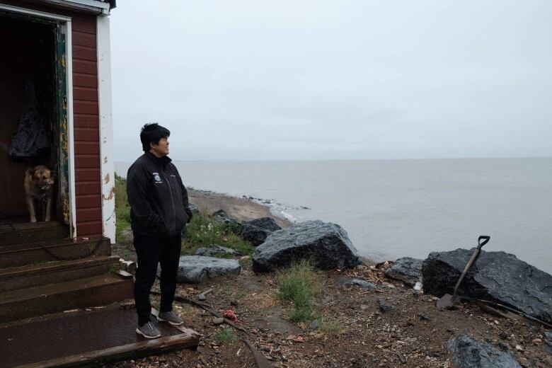 A woman stands on the steps of a home near the seashore.