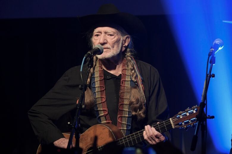 A man holding a guitar stands in front of a microphone performing.